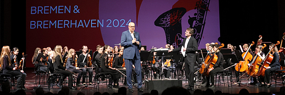 Bürgermeister Andreas Bovenschulte  steht auf der Bühne und spricht beim Orchesterfestival in Bremerhaven 2024. 